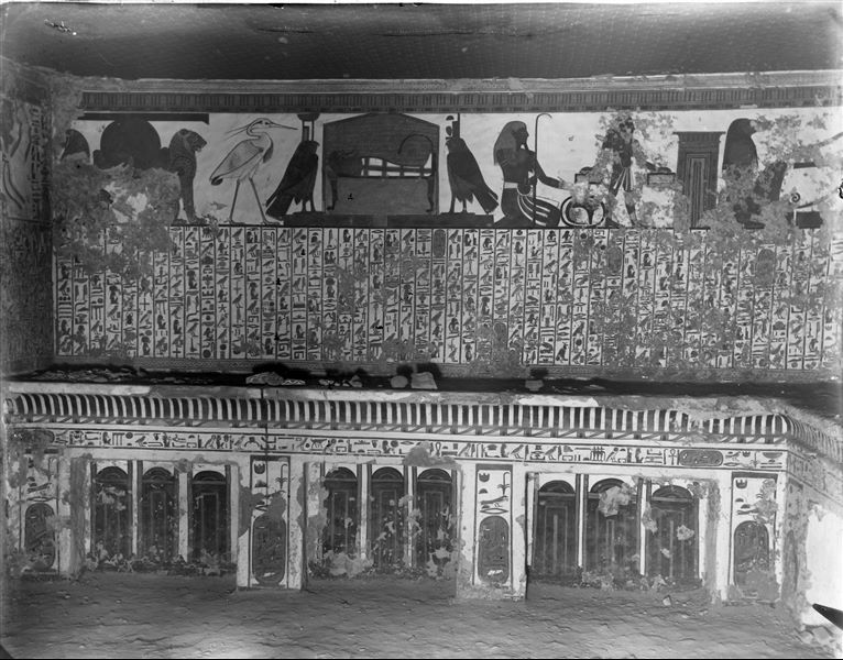 View of the antechamber, west wall, scene 3. Represented in the upper register: Atum between two lions, the Benu bird, the mummy (of Nefertari) on a bed between two falcons which represent the goddesses  Nephthys and Isis. These are representations connected with the central register, which presents Spell 17 of the Book of the Dead. Below, represented on the left is a decoration composed of Djed pillars and Tit knots, while in the centre there is a cavetto cornice, with representations of sanctuaries. Also visible is the ceiling painted with stars. 