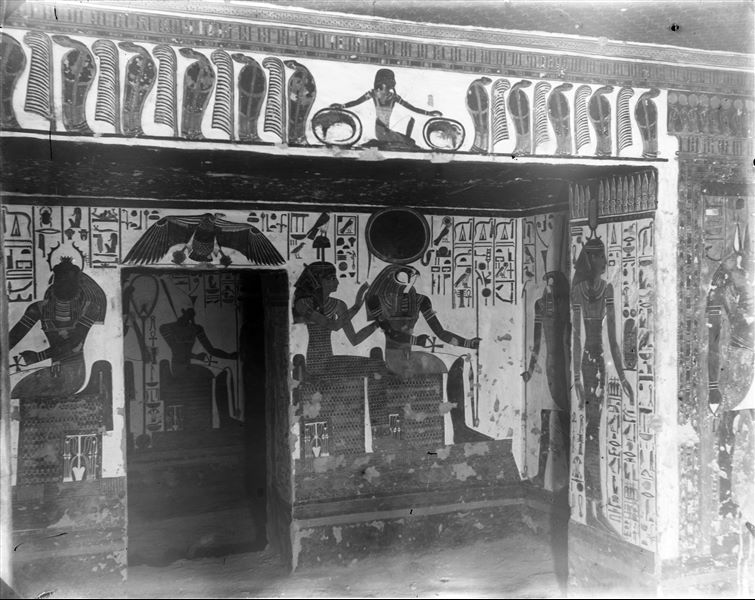 View of the vestibule, in the direction of the first eastern annex (alcove). Particularly visible is the south-east corner, scenes 7 and 8 .The god Horus leads Nefertari (not visible here, scene 7) towards two seated gods, Ra-Horakhty and Hathor (scene 8). On the right, corresponding to the entrance of the vestibule, the goddess Neith is visible (scene 6) looking towards the antechamber. In the foreground, the lintel of the entrance to the vestibule is decorated with eleven uraeus-serpents alternating with eleven blue ostrich feathers and a kneeling deity in the centre. Photograph taken from the antechamber. 