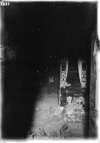 Fotografia scattata imperfettamente, si riconosce ugualmente la parte centrale della camera funeraria, con i tre gradini che conducevano al sarcofago, al centro della stanza, e il pilastro D, lato a, rappresentante il pilastro Djed. Si nota, in primo piano, la presenza di frammenti e/o detriti.