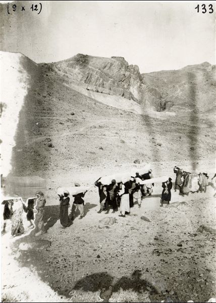 Transporting the coffins found in the tombs of Prince Sethiherkepshef (QV 43) and Prince Khaemwaset (QV 44) in the Valley of the Queens towards Luxor, during the Italian Archaeological Mission’s excavations. In the background, there are the four tombs excavated in the so-called “Valley of Prince Ahmose”. Schiaparelli excavations. 