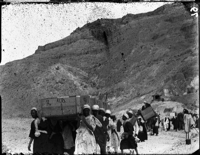 Transporting crates from the camp in the Valley of the Queens to the Nile, during the final stages of the excavation. Notable on the right is a camera covered by a cloth. Schiaparelli excavations.