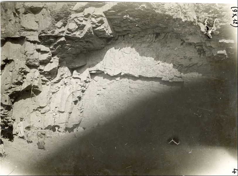 Momento di scavo di una tomba non terminata in una parete rocciosa. La fotografia risulta sovraesposta nella parte inferiore destra. Scavi Schiaparelli.