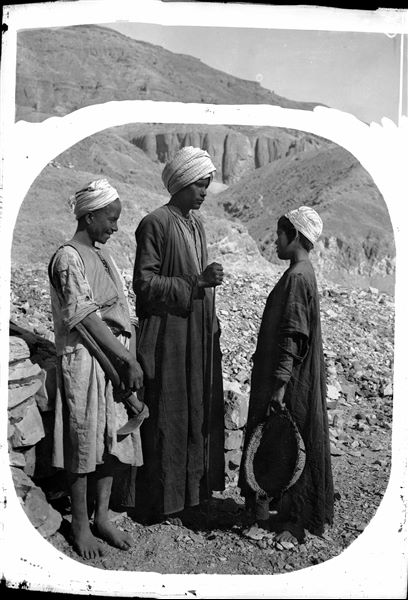 Giovani operai fotografati in un momento di pausa, sullo sfondo, il vallone attiguo alla Valle delle Regine. Scavi Schiaparelli.