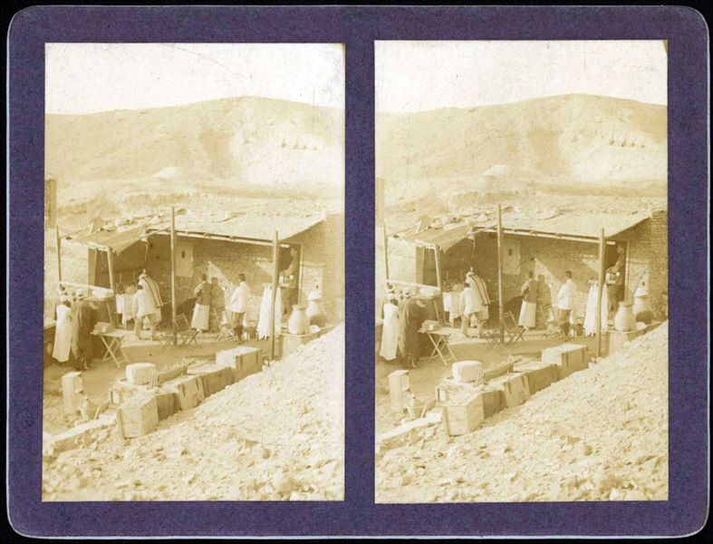 Casupola dell’accampamento della Missione Archeologica Italiana nella Valle delle Regine nel 1906, durante la celebrazione della Messa. L’unico personaggio riconoscibile è Bolos Ghattas, dragomanno della missione, alle spalle del sacerdote e appoggiato al muro della casupola. Sullo sfondo, sulla destra, si vedono le quattro tombe scavate già nel 1903, nell’area chiamata “valletta del principe Ahmose”. 