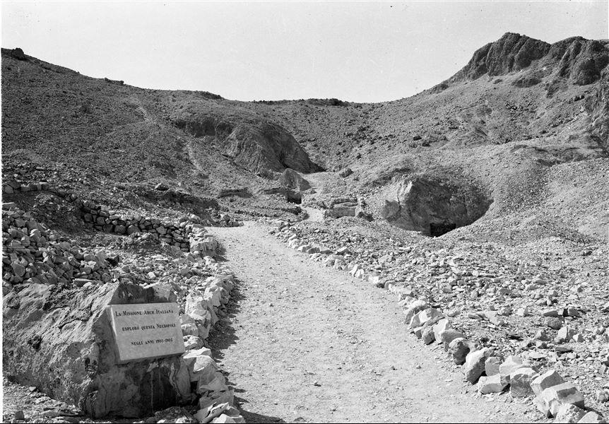 View of the last section of the Valley of the Queens. Visible from right to left are the entrances to tombs QV45, QV44 (of Prince Khaemwaset) and QV43 (of Prince Setiherkhepeshef). In the foreground, the plaque commemorating the Italian excavations in the Valley, followed by the barely visible shaft of the tomb of Princess Ahmose (QV47). Schiaparelli excavations.