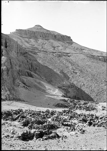 Resti archeologici, da ulteriore angolazione, del cosiddetto “Villaggio del colle”. Si riconosce sullo sfondo il picco della montagna El-Qurn, il punto più alto della montagna tebana. Scavi Schiaparelli.