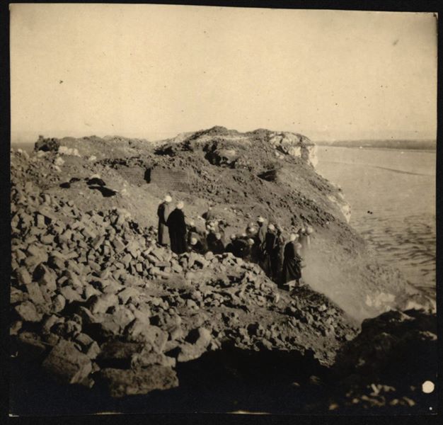 Workers on the southern hilltop where the fortress and the temple dedicated to the goddess Hathor stood. On the right, in addition to the crops, the Nile is visible. The figure in light clothing, beside the ghaffir (guard/watchman) could be Virginio Rosa, or Michelangelo Pizzio. Schiaparelli excavations.