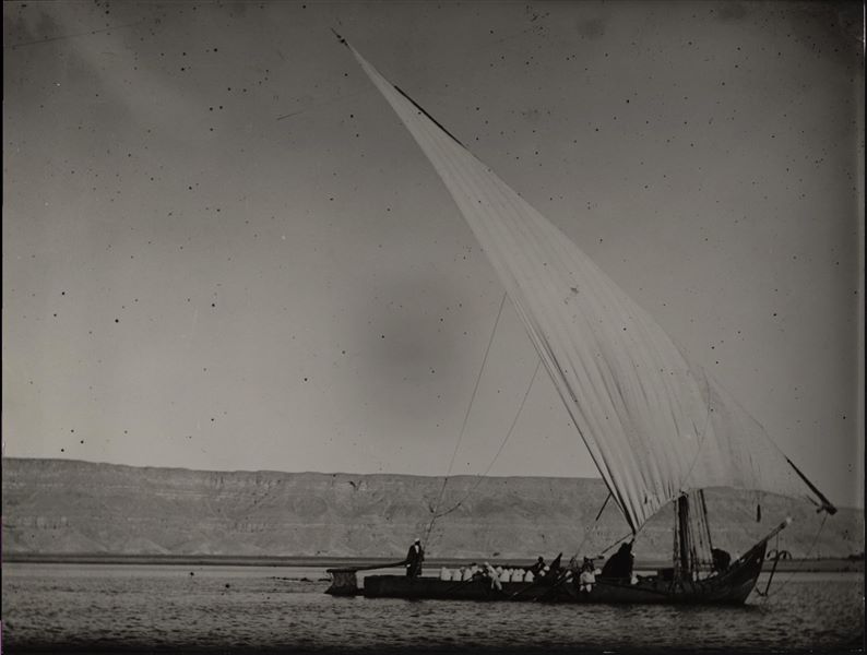 The Nile at Gebelein, in addition to the large felucca on the Nile, in the background on the opposite side of the river, the archaeological site of Mo’alla is visible. Schiaparelli excavations.
