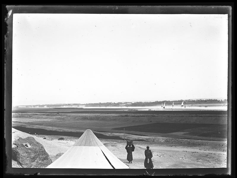  At the bottom towards the left, two Egyptians can be seen next to a tent belonging to the Italian Archaeological Mission, in Gebelein. In the background, some boats sailing on the Nile River. Schiaparelli excavations.