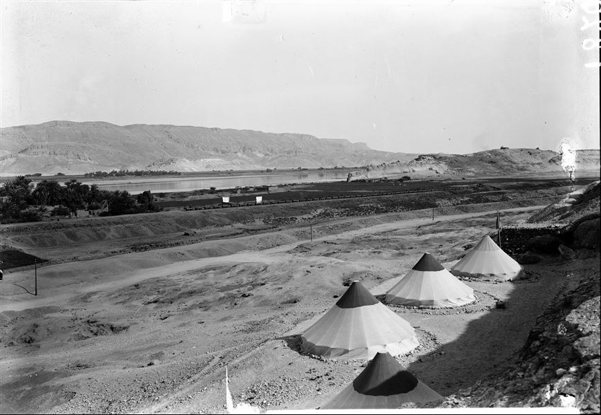 Camp of the Archaeological Mission. The picture taken from the top of the hill makes it possible to appreciate the panorama: in the background, the mountain range of the Eastern Desert, the Nile and the small narrow-gauge railway used to transport sugar cane. On the right, the southern hill with the tomb of the saint Sheikh Musa on its summit. Schiaparelli excavations. 