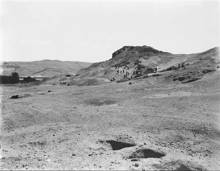 Continuation of excavations along the northern slope of the hill. Visible in the foreground are tomb shafts and brick structural remains, still buried. On the right, Giulio Farina under a white parasol. Farina excavations. 