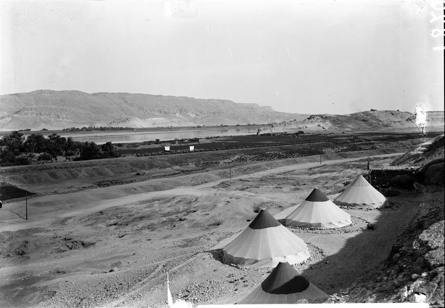 Camp of the Archaeological Mission. The picture taken from the top of the hill makes it possible to appreciate the panorama: in the background, the mountain range of the Eastern Desert, the Nile and the small narrow-gauge railway used to transport sugar cane. On the right, the southern hill with the tomb of the saint Sheikh Musa on its summit. Schiaparelli excavations. 