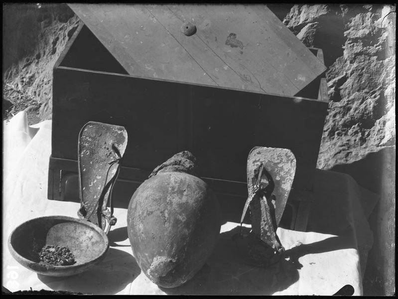 Tomb of the Unknown. Before being packed for transport, the objects were inventoried and photographed, often grouped together. Visible in the picture: a chest with a lid (S.13986); a stone bowl (S.14039); a terracotta vase with a mud cap (S.13996) and a pair of leather sandals (S.14043). Schiaparelli excavations. 