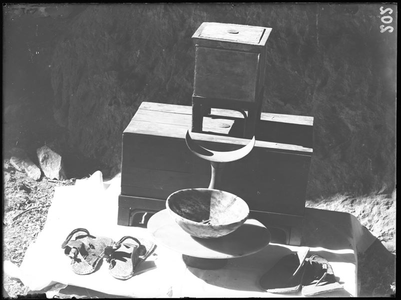 Tomb of the Unknown. Before being packed for transport, the objects were inventoried and photographed, often grouped together. Visible in the picture: two chests with lids (S.13986 [the larger one] and S.13985); an alabaster dish (S.14040); a stone bowl (S.13970); a wooden headrest (S.14042) and 2 pairs of leather sandals (S.14045 and S.14044). Schiaparelli excavations.