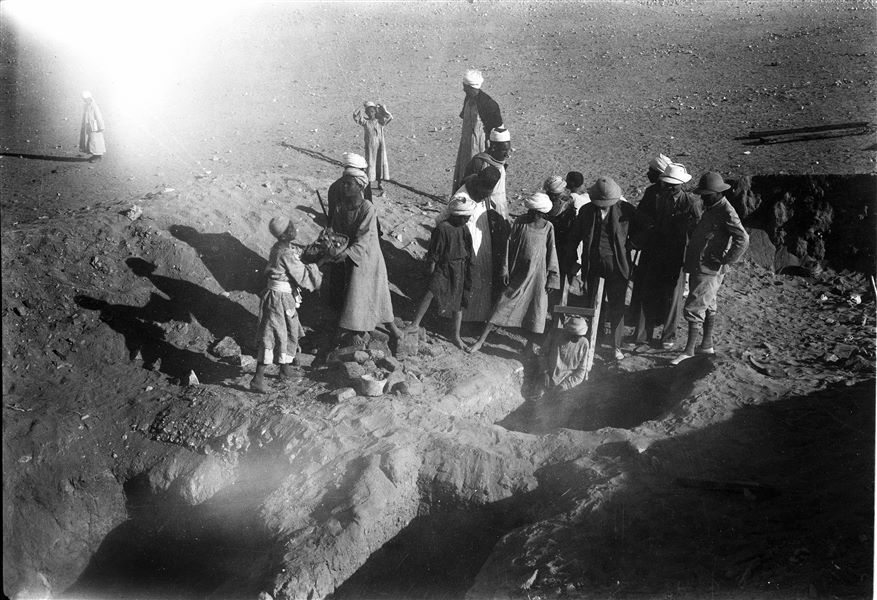 Excavation area overlooking the village of Abu Hummas. Workers are removing the excavated material from one of the shafts visible in image B00559. Identifiable starting from the left: Giovanni Marro, Michelangelo Pizzio and Giulio Farina. Farina excavations. 