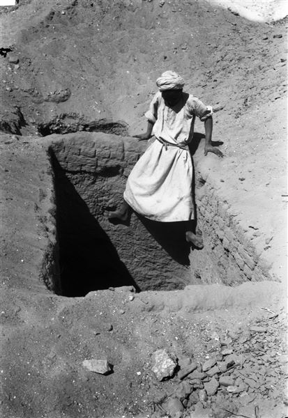 Accesso del pozzo visibile in B00607, un giovane operaio indica la modalità di discesa e salita, utilizzando i punti di appoggio anticamente ricavati nella muratura. Scavi Farina.