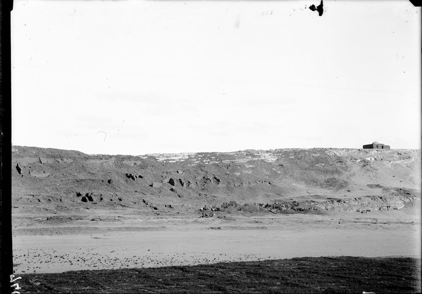 General view of the western side of the southern hill. Workers are engaged in excavations at the bottom of the valley. Along the mountainside are the significant mud-brick structures; the subject of subsequent research. At the top right, the tomb of the holy man Sheikh Musa. Schiaparelli excavations. 