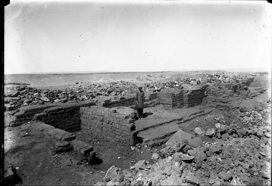 Sommità della collina sud. Resti del tempio dedicato alla dea Hathor. A fianco della persona si vede una grossa base per una colonna in pietra. Sullo sfondo si profila la collina nord. Scavi Schiaparelli. 