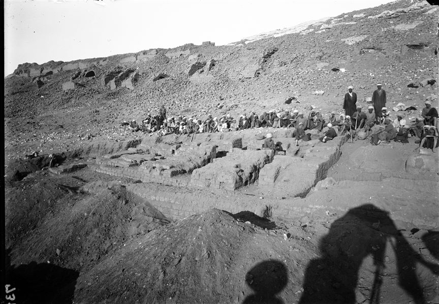Excavations at the foot of the southern hill, western side. To the right of the large mud-brick structure are two large vessels still partially buried, probably for the storage of grain. Behind the workers are the figures of two supervisors. Schiaparelli excavations. 