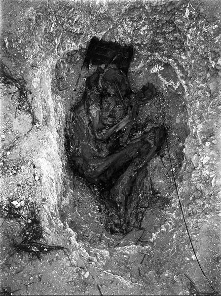 ​Scattered burials in the desert area north of the northern hill. The deceased, already depicted in photograph DD00109, was wrapped in a mat in a contracted position. Traces of the mat still remain on the body. A ceramic fragment containing some unidentifiable spherical objects was placed near the deceased’s head. Farina excavations. 