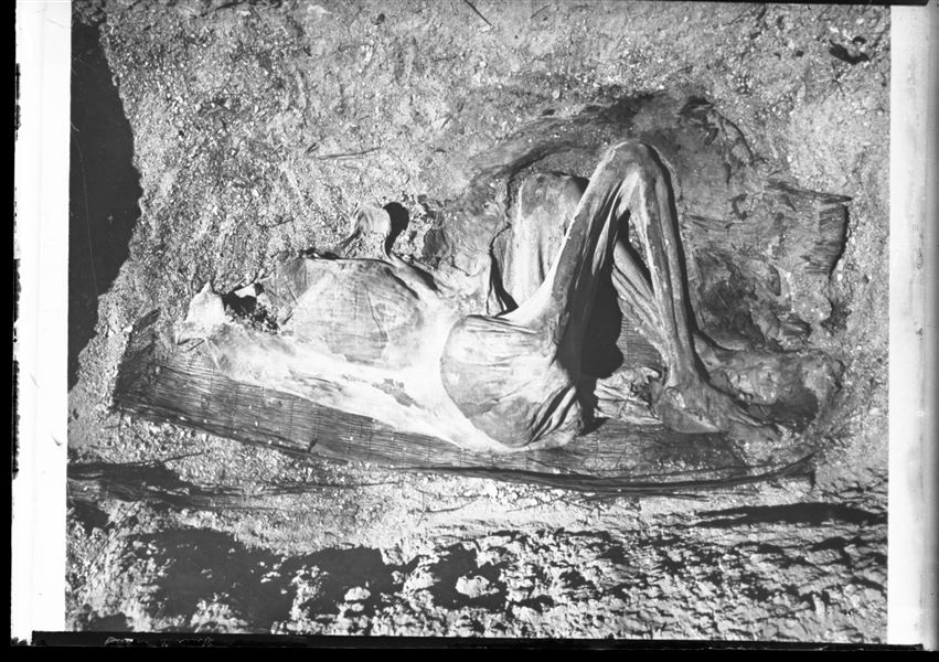  Burial with a naturally mummified human body lying on a mat in a crouched position. The body is missing its skull, part of the upper torso and the upper limbs.