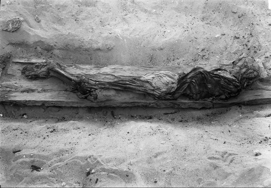 Burial of a young individual in a rectangular coffin, only the bottom has been preserved. The deceased, wrapped in cloth, is lying on its side. Schiaparelli excavations. 