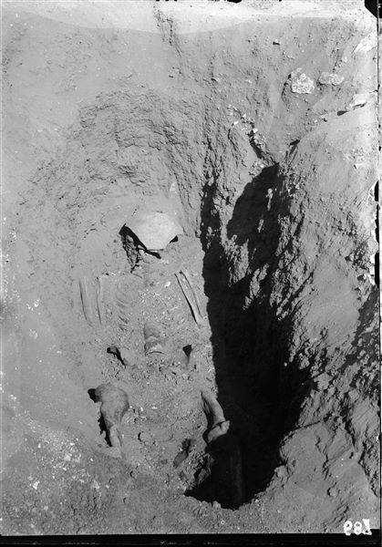 Burials in the plain to the east of the northern hill. The deceased, lying down and apparently without traces of a sarcophagus, has its skull covered with a ceramic fragment. Schiaparelli excavations.  