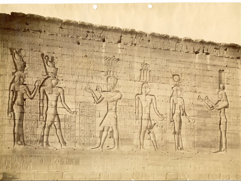 The photograph depicts the exterior of the north perimeter wall of the Temple of Horus at Edfu, where sacred scenes of presenting offerings to the gods are carved. Based on the calligraphic style, the photograph can be attributed to Antonio Beato. 