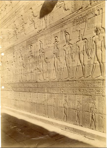 The photograph depicts sacred scenes from the interior walls of the Temple of Horus at Edfu. The author's signature is visible at the bottom left.