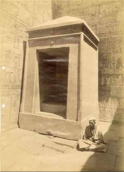 The photograph depicts a local resident seated next to the large naos (shrine) of Pharaoh Nectanebo II inside the Temple of Horus at Edfu. It is the oldest element of the temple visible today, and is believed to have originally contained an effigy of the god Horus. 