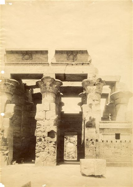 The photograph offers a view of the interior of the hypostyle hall of the Temple of Sobek and Haroeris at Kom Ombo, seen frontally from the entrance to the sanctuary.  The image displays the mirrored signature of the author at the bottom right.