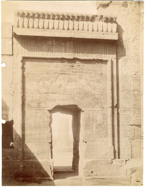 The photograph shows a close-up of the left-side door in the Temple of Sobek and Haroeris at Kom Ombo, photographed from inside the temple. The author's signature, almost entirely cut off, is still recognisable at the bottom left. 