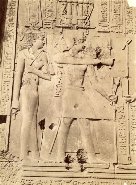 The image shows a detail of relief decoration on the walls of the Temple of Sobek and Haroeris at Kom Ombo. It shows Ptolemy VIII Euergetes II and one of the Cleopatras (Cleopatra II or III, both were consorts of Ptolemy VIII) performing a ritual to honour a deity (here not in frame). Based on the calligraphic style of the caption, it is possible to attribute the shot to Antonio Beato. 