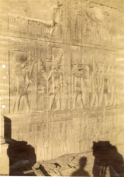 La fotografia propone alcune scene dalle pareti del tempio di Sobek e Haroeris a Kom Ombo, nelle quali il faraone Tolomeo VIII è al cospetto delle divinità. In basso è riconoscibile l’ombra del fotografo e della macchina fotografica. 