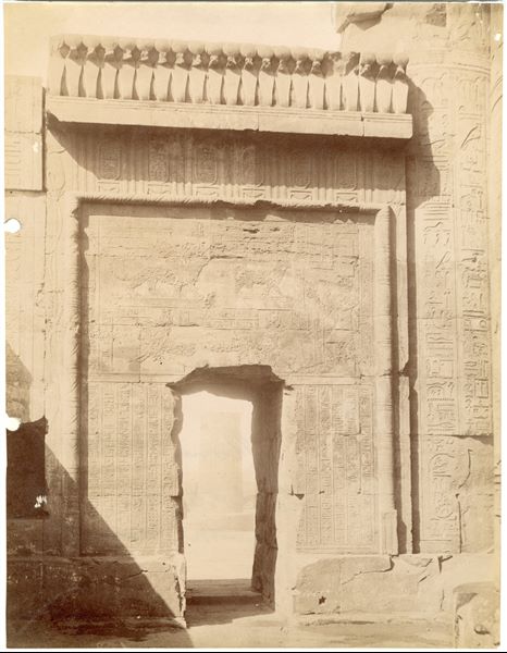 The photograph shows a close-up of the left-side door in the Temple of Sobek and Haroeris at Kom Ombo, photographed from inside the temple. The author's signature, almost entirely cut off, is still recognisable at the bottom left. 