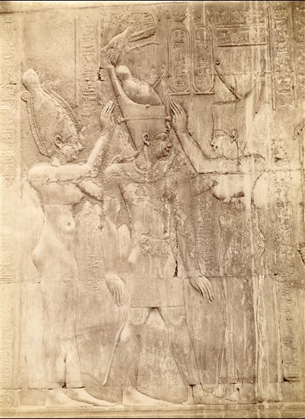 The photograph illustrates a sacred scene from the interior walls of the Temple of Sobek and Haroeris at Kom Ombo, where Pharaoh Ptolemy XII is purified by two female deities, in the presence of Ra-Horakti (not visible in this picture) on the right. 