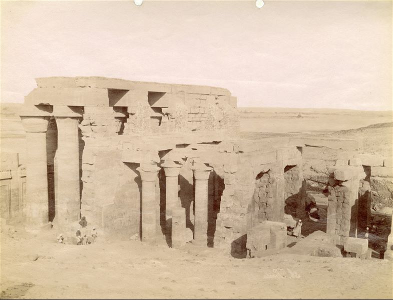 La fotografia presenta la veduta da est dell'atrio colonnato esterno (sinistra) e di quello interno (al centro) del tempio di Sobek e Haroeris a Kom Ombo. più a destra si notano anche le rovine della Sala delle Offerte. La firma dell'autore è posta in basso a destra, in grafia speculare.