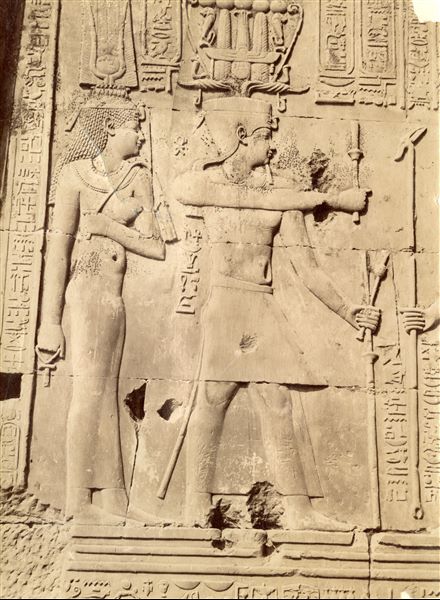 The image shows a detail of relief decoration on the walls of the Temple of Sobek and Haroeris at Kom Ombo. It shows Ptolemy VIII Euergetes II and one of the Cleopatras (Cleopatra II or III, both were consorts of Ptolemy VIII) performing a ritual to honour a deity (here not in frame). Based on the calligraphic style of the caption, it is possible to attribute the shot to Antonio Beato. 