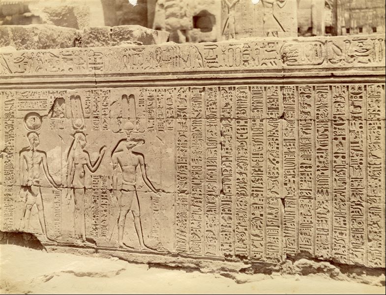 The photograph depicts a scene and text from the external wall of the hypostyle hall (visible in the background) of the Temple of Sobek and Haroeris at Kom Ombo. 