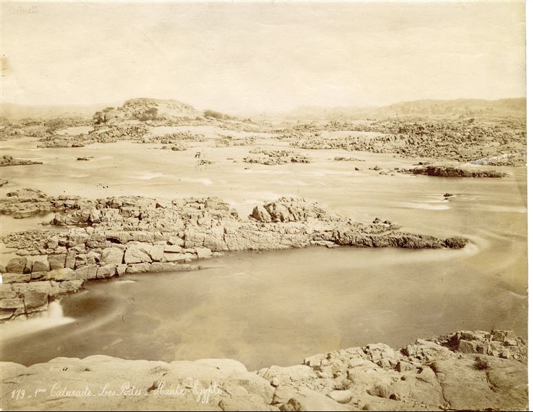 Il panorama fotografato presenta le rapide della Prima Cateratta del Nilo nei pressi di Assuan e il paesaggio roccioso dell'Alto Egitto. In basso a sinistra la firma dell’autore.