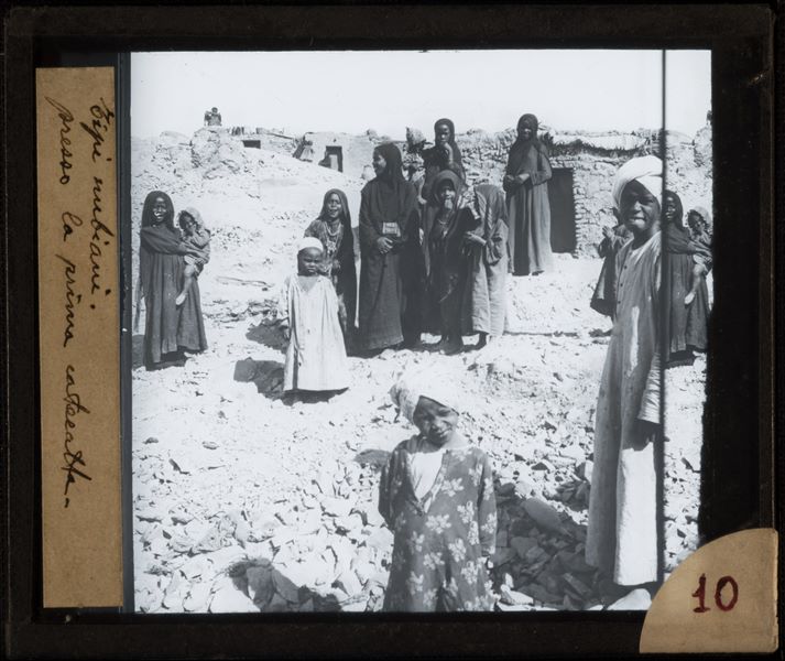 Group of Egyptians posing at the First Cataract in Aswan, with housing constructed of raw earth in the background.