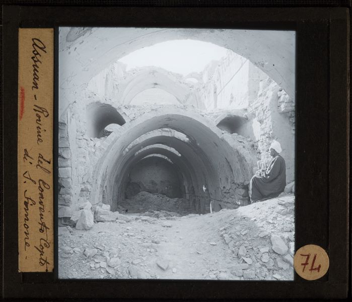 Ruins of the Monastery of St. Simeon at Aswan. On the right, an Egyptian is photographed, posing seated.