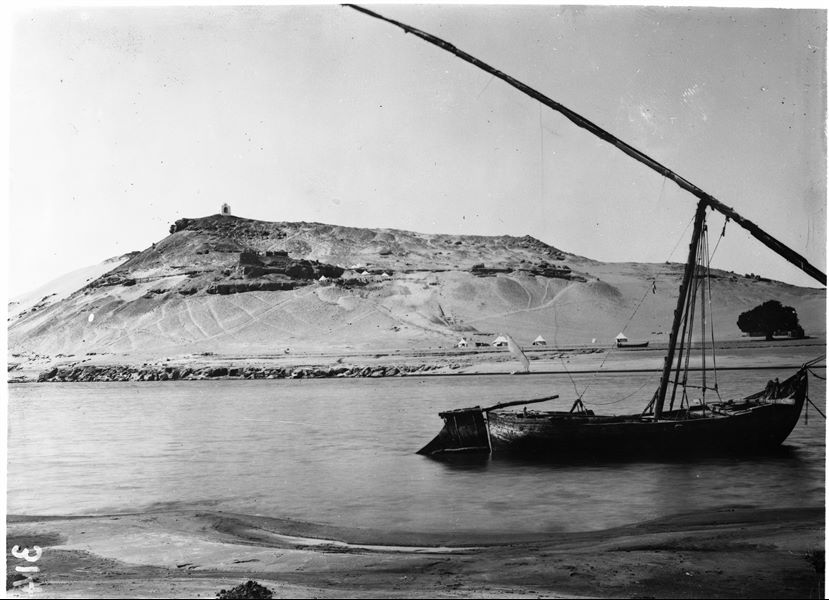 Veduta del versante settentrionale della necropoli rupestre della Qubbet el-Hawa fotografata dall’altra riva del Nilo. Si riconosce, a mezza costa, l’accampamento della missione. Scavi Schiaparelli.