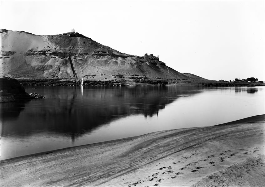 Veduta del versante meridionale della necropoli rupestre della Qubbet el-Hawa, fotografata dall’altra riva del Nilo. Si riconosce, al centro, la rampa della tomba di Sabni I, già portata alla luce. In cima, la tomba musulmana dello sceicco Ali el-Hawa. Scavi Schiaparelli.