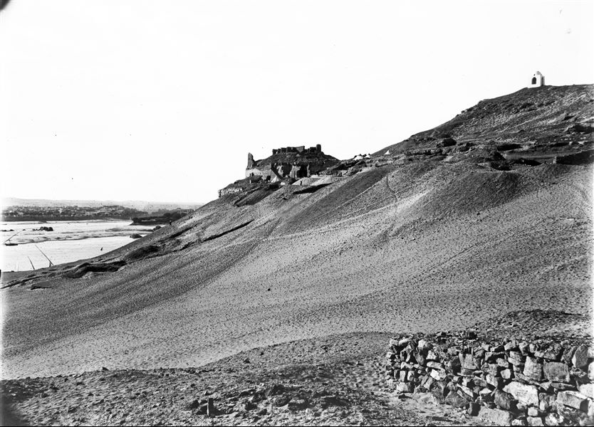 View of the northern slope of the Qubbet el-Hawa rock-cut tombs, photographed from the other side of the Nile. The mission’s camp can be seen halfway up the hill. Schiaparelli excavations.