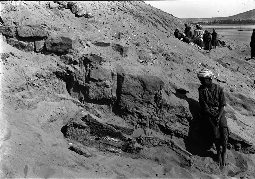 Discovery of a skeleton with remains of a wooden coffin, photographed from a northerly direction, during excavations in Qubbet el-Hawa. In the background, the Nile. Schiaparelli excavations.
