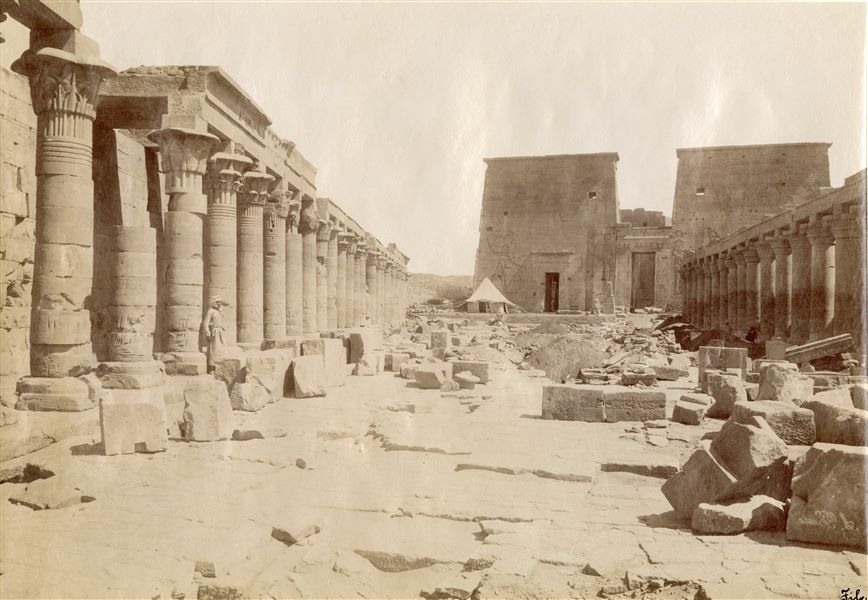 L'immagine mostra una veduta complessiva dell’accesso (lato meridionale) del complesso templare dedicato alla dea Iside sull’isola di File. Si notano il cortile, i colonnati laterali e il pilone d'accesso. Davanti al pilone è presente una tenda bianca conica. La firma dell'autore è posta in basso a destra, con grafia speculare.  