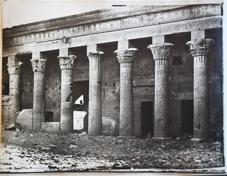 The photograph shows the colonnaded portico of the Temple of Isis at Philae, in the first court. The ground level still covers the  columns’ bases. An icorrect indication that this is the temple of Dakka has been placed at the bottom left. The author's signature is visible at the bottom right.
