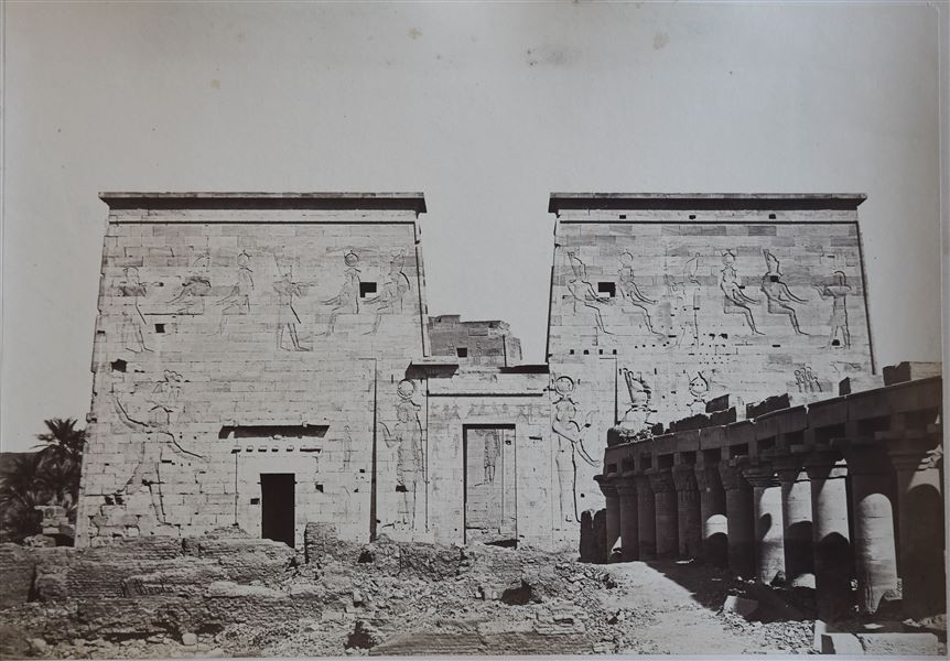 La fotografia mostra il I pilone e il cortile colonnato antistante, del tempio di Iside sull’isola di File. Da notare la presenza di piccoli edifici in mattoni di epoca successiva, costruiti su un piano di calpestio che copre ancora la parte inferiore delle colonne antiche.  