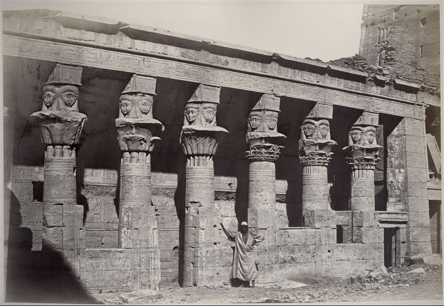 Detail of the temple complex of Isis on the island of Philae, where the portico of the Mammisi is photographed, with columns with Hathoric capitals, still partially covered by a layer of earth and sand. The Mammisi is a building constructed in the Late and Greco-Roman periods, positioned next to a major temple to celebrate the mysteries of divine births. The author's signature is at the bottom right.